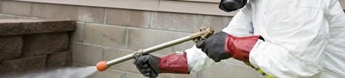 Pest control technician applying exterior insect treatment along a home foundation in Fort Lauderdale, FL
