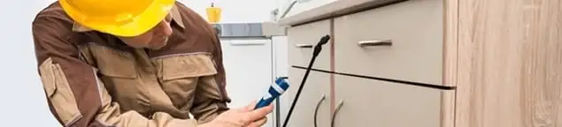 Roach exterminator applying treatment under kitchen cabinets in Fort Lauderdale, FL