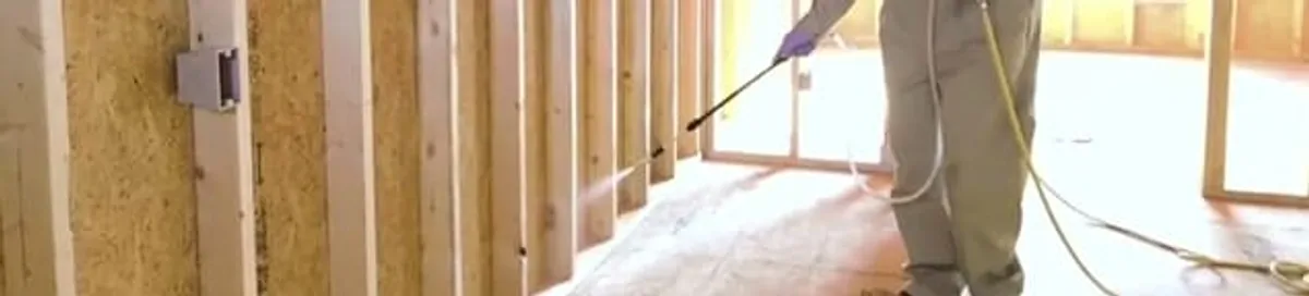 Termite treatment technician applying spray along framing and unfinished walls in Fort Lauderdale, FL