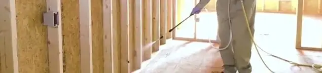 Termite treatment technician applying spray along framing and unfinished walls in Fort Lauderdale, FL